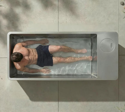 Top-down view of man in outdoor cold plunge tub with clear water, demonstrating ice bath recovery and cold exposure in a modern backyard setting