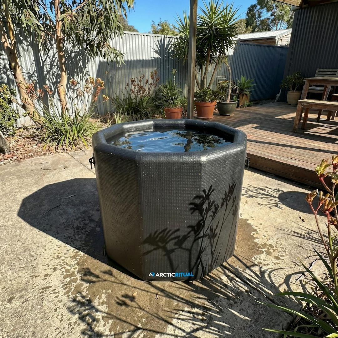 Arctic Ritual Lite+ Barrel cold plunge tub in black set outdoors in a sunny backyard, compact octagonal ice bath for home recovery and cold exposure therapy.