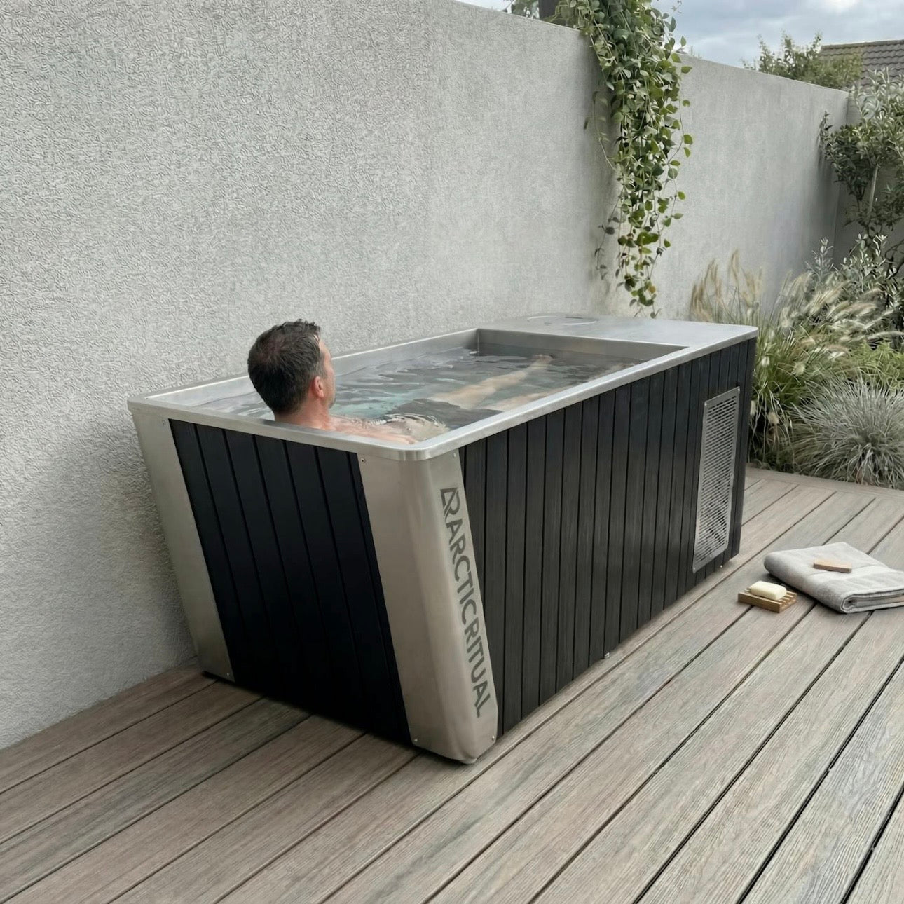 Person relaxing in Arctic Ritual Platinum All-In-One cold plunge tub with black exterior and stainless steel interior outdoors