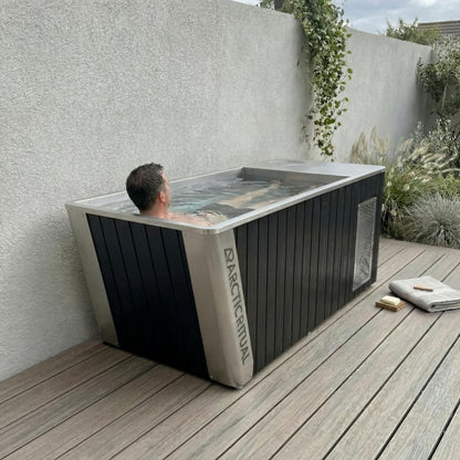 Person relaxing in Arctic Ritual Platinum All-In-One cold plunge tub with black exterior and stainless steel interior outdoors